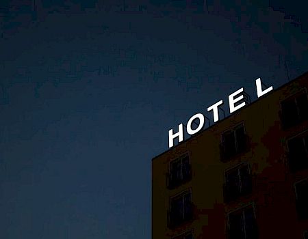 The image shows a building with a "HOTEL" sign at the top against a dark sky, with the letter "E" unlit.