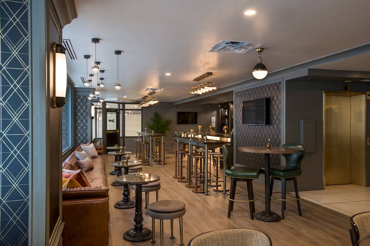 This image shows a modern lounge with seating areas, high tables, bar stools, and stylish lighting fixtures in a contemporary setting.