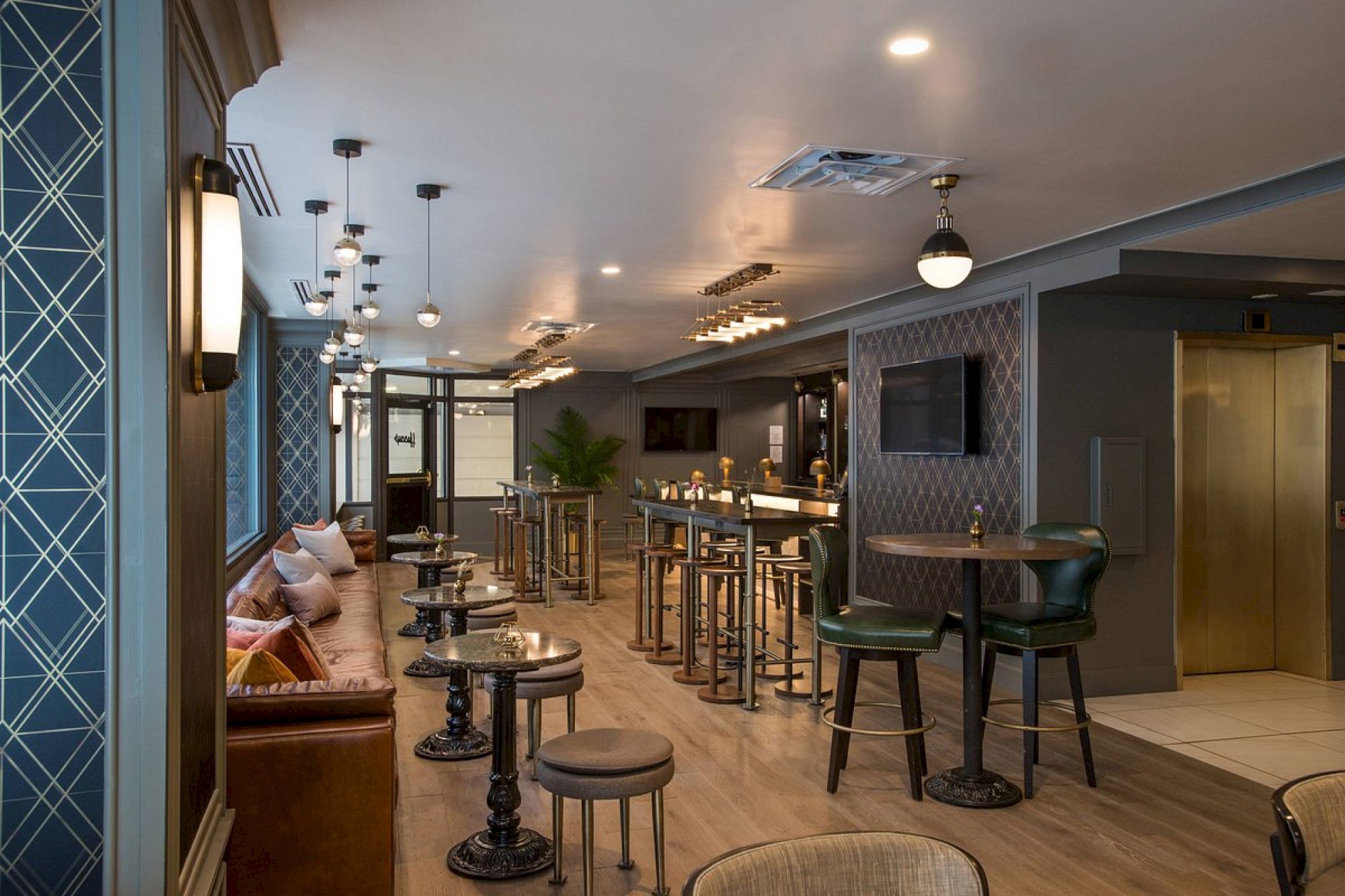 This image shows a modern lounge with seating areas, high tables, bar stools, and stylish lighting fixtures in a contemporary setting.