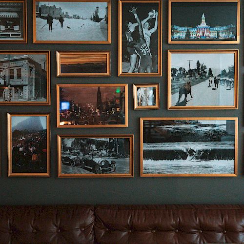 A wall with an eclectic collection of framed photos of various scenes, including landscapes and people, above a brown leather couch.