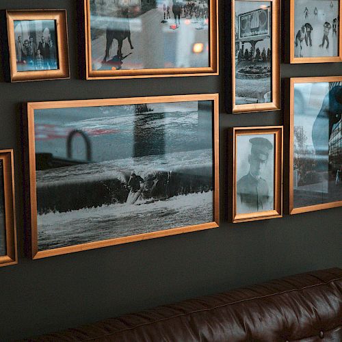 The image shows a wall with various framed photographs and a brown leather couch below them, creating a gallery-style display.