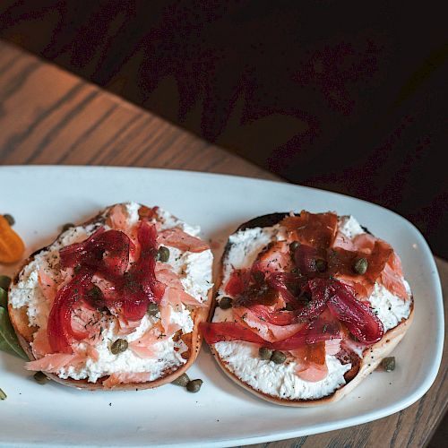 The image shows a plate with two bagels topped with cream cheese and what appears to be smoked salmon or similar toppings, placed on a wooden table.