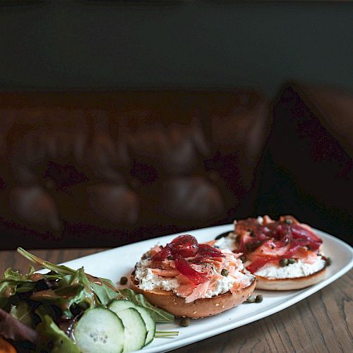 A rectangular plate with a salad featuring cucumber slices and two pieces of toast topped with various ingredients, placed on a wooden table.