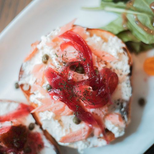 A plate with bagels topped with cream cheese, smoked salmon, capers, onion, alongside a side salad with dressing.