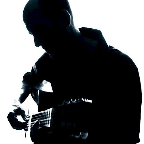 The image shows a silhouette of a person playing an acoustic guitar against a backlit background. The details of the person are not visible.