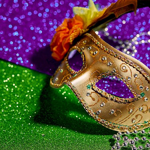 The image shows a decorated half-face mask, embellished with beads and flowers, set against a sparkling green, purple, and yellow backdrop, resembling Mardi Gras.