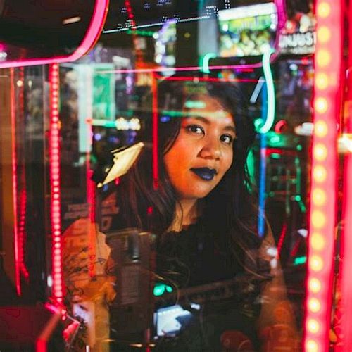 A woman is seen through colorful neon lights, reflecting an urban, vibrant atmosphere.