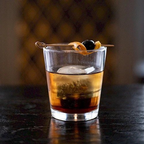 A glass of whiskey on a dark bar, with a twist of citrus peel garnish resting on top.