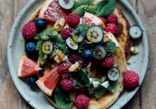 Colorful fruit-tlecked pancakes topped with kiwi, berries, grapefruit, mint on a rustic plate and wooden table, fresh and vibrant.