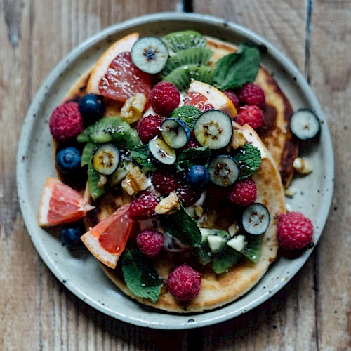 Colorful fruit-tlecked pancakes topped with kiwi, berries, grapefruit, mint on a rustic plate and wooden table, fresh and vibrant.