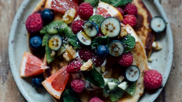 Colorful fruit-tlecked pancakes topped with kiwi, berries, grapefruit, mint on a rustic plate and wooden table, fresh and vibrant.