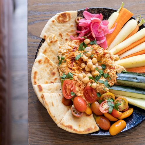A veggie platter with pita bread, creamy spread, chickpeas, and sliced carrots, cucumbers, zucchini, and tomatoes.
