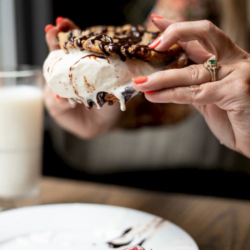 A hand picks a bite from a chocolate-drizzled cake slice topped with creamy frosting.